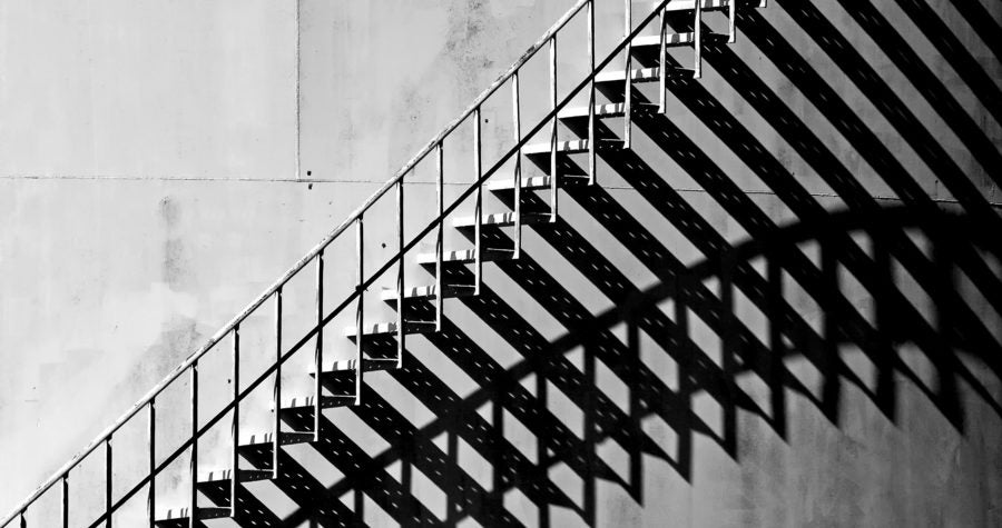 Heavy shadow of stairway on old white storage tank. Stairs cast interesting shadows in the late afternoon Sunlight. Black and White