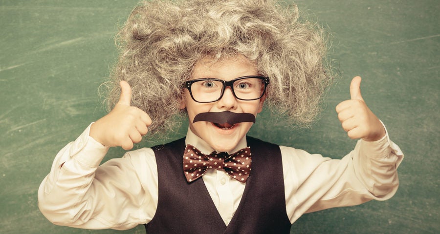 Cheerful smiling little kid (boy) against chalkboard. Looking at camera. Little Einstein style. School concept