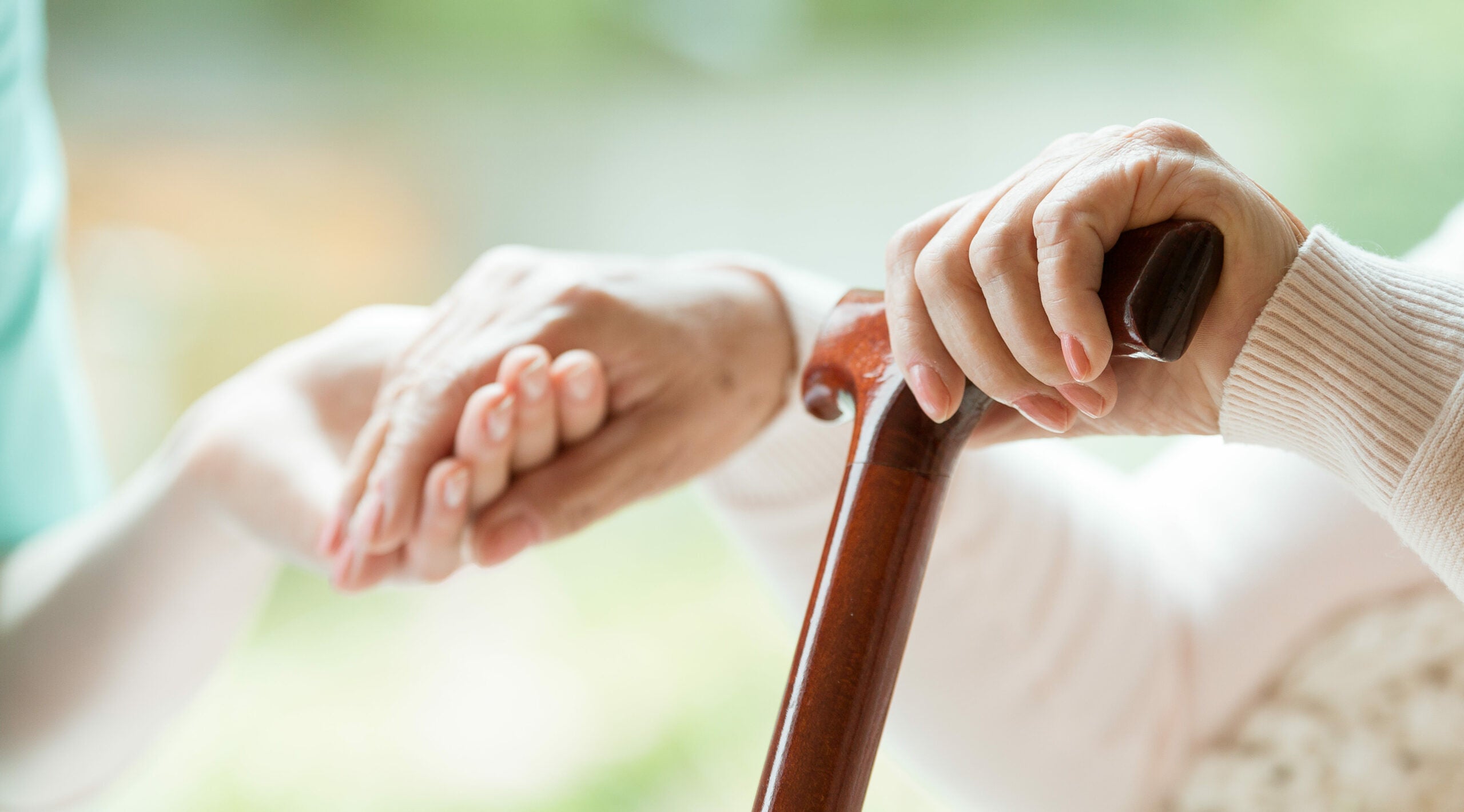 Elder person using wooden walking cane during rehabilitation in friendly hospital.