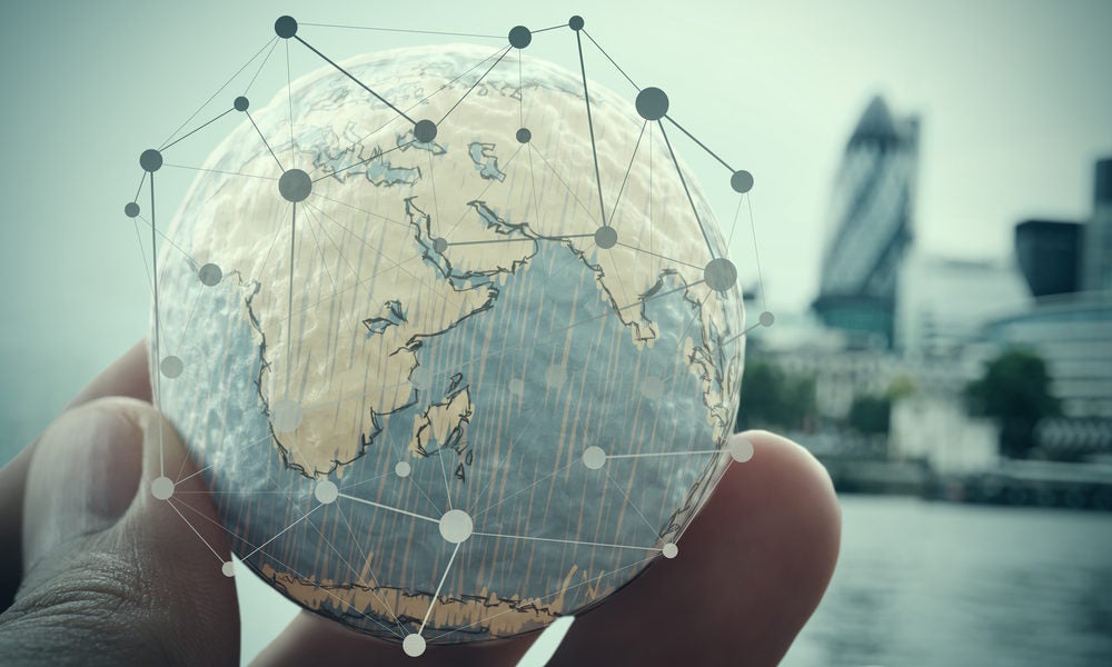 Hand holding miniture world globe with network image overlaid. Modern city skyline in background.