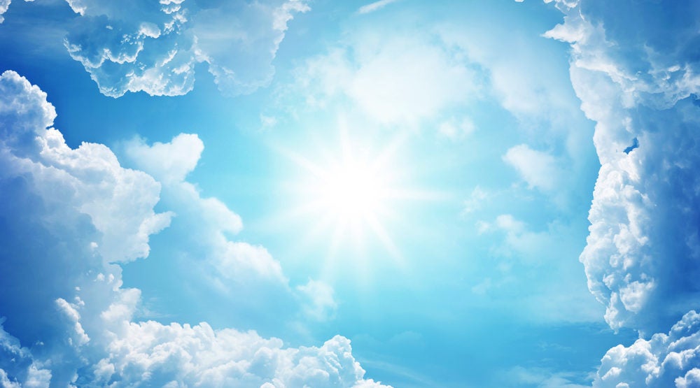 Sun centered in cicle of fluffy white clouds in a blue sky.