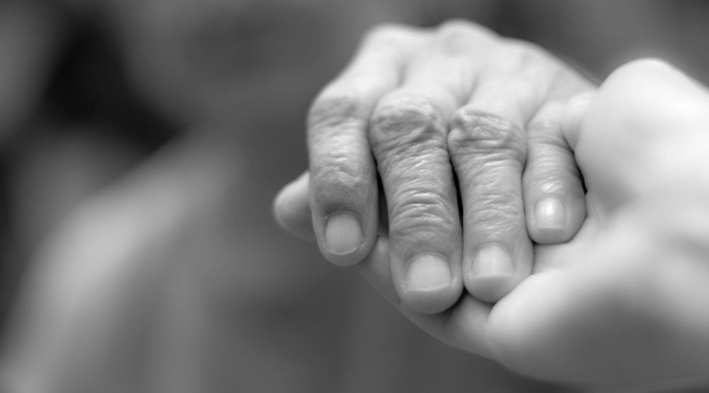 Old woman holding hand of younger care giver, in black and white.